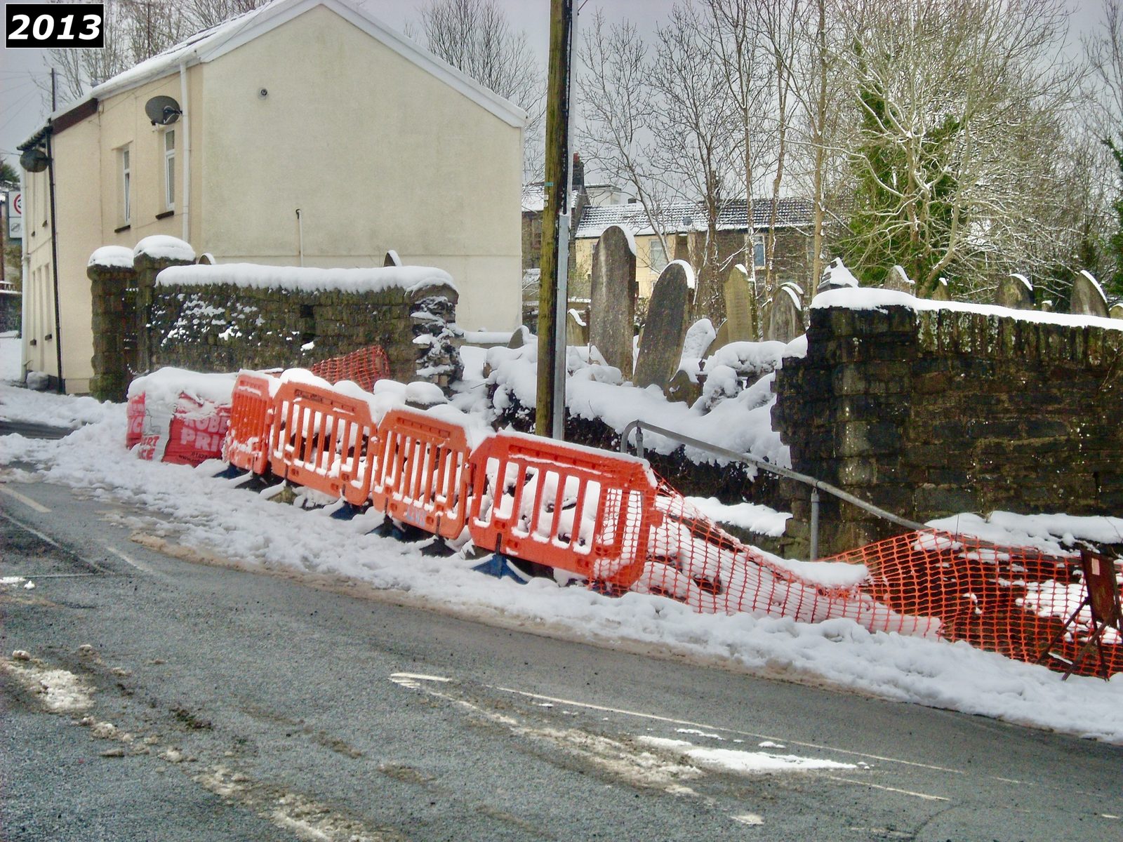 Saron graveyard boundary wall in the snow in 2013, with red safety barriers in place during works