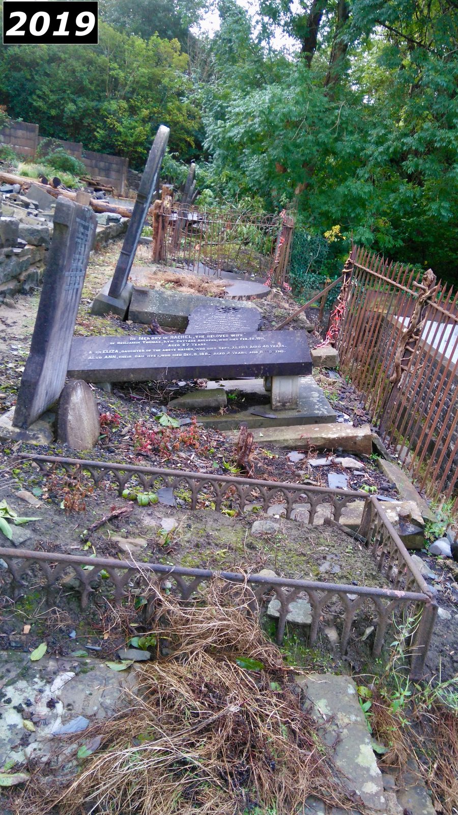 Leaning and collapsed headstones behind fencing at Saron graveyard in 2019