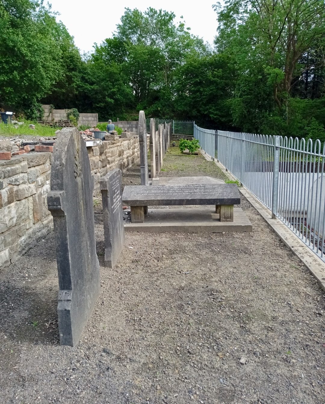 Restored upright headstones and a table tomb beside the new blue railing at Saron in 2024, with a gravel path laid