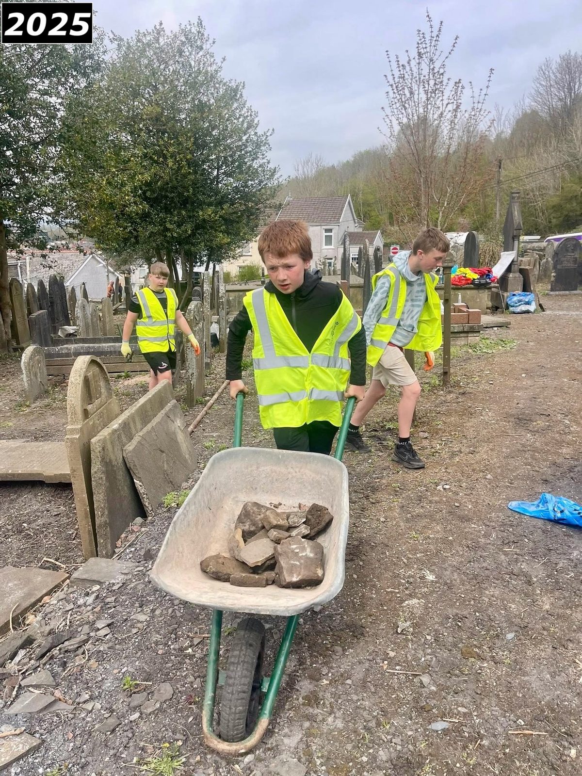 A young volunteer moving a wheelbarrow during a work day at Saron graveyard in 2025