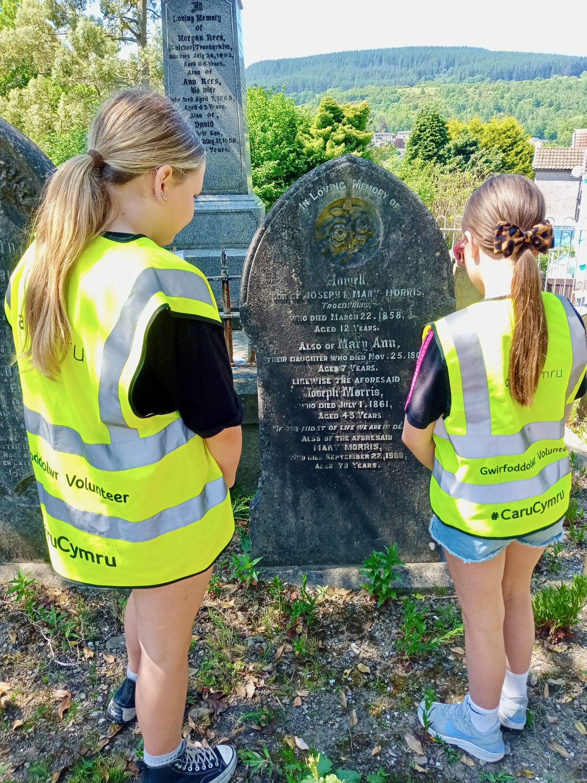 Two young volunteers in hi-vis vests reading an inscription on a restored headstone at Saron graveyard